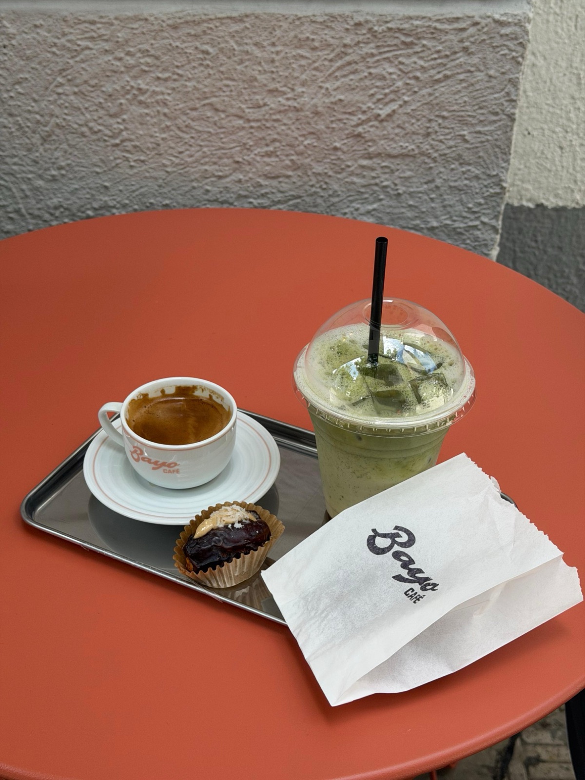 Espresso, matcha gelado e tâmara recheada numa mesa laranja, com a embalagem da BAYO Café